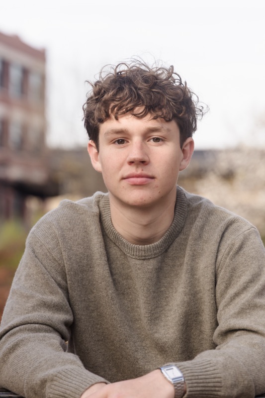 Young man with curly hair in a gray sweater on a city street