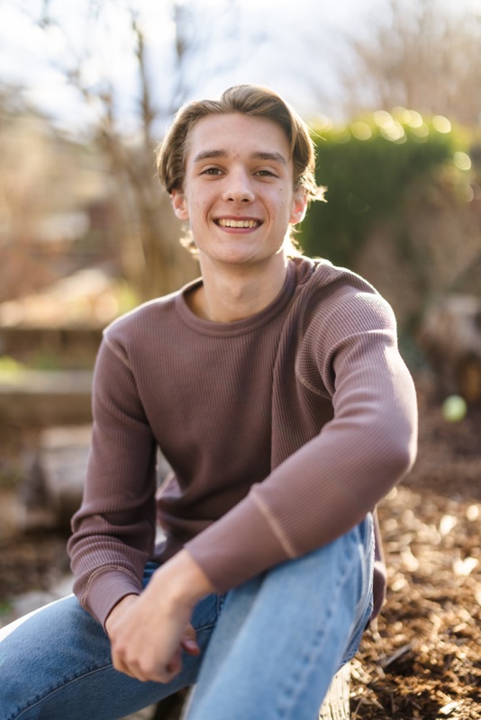 Smiling young man in a mauve sweater kneeling in a garden