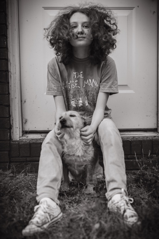 Black-and-white portrait of a young woman with curly hair on a doorstep with her dog