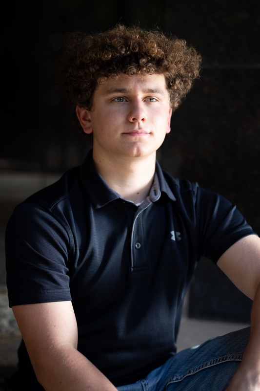 Young man with curly hair in a black polo shirt in strong side light
